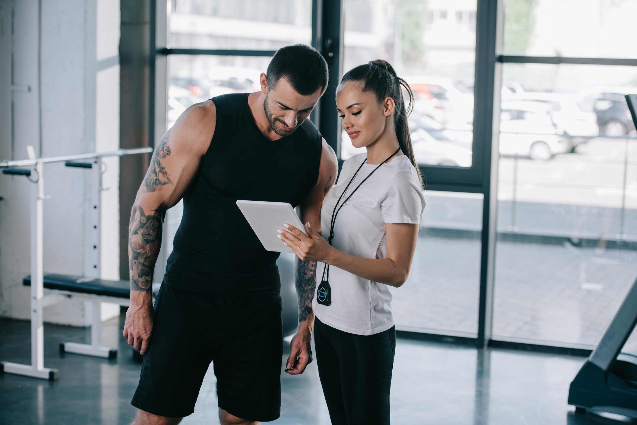 female personal trainer and sportsman looking at screen of digital tablet at gym